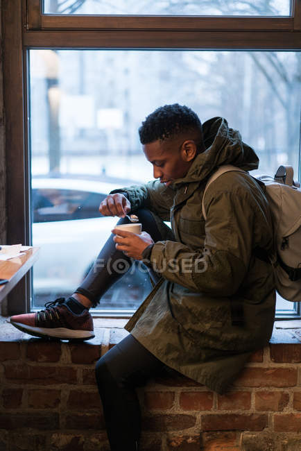 Side view of tourist man drinking coffee on window sill in cafe. — Stock Photo