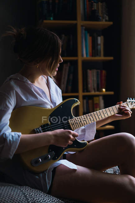 Side view of woman playing guitar on coach — Stock Photo