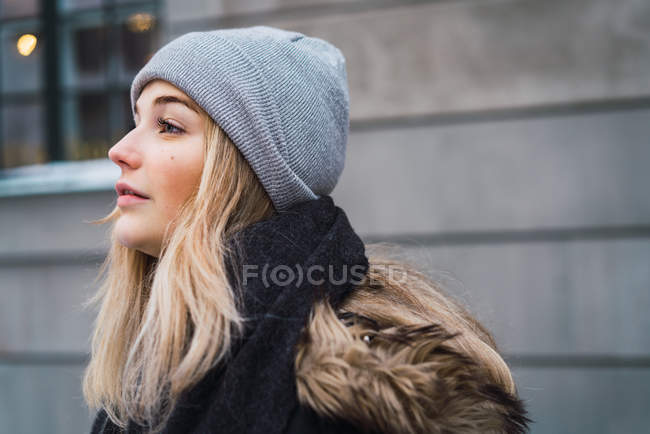 Vista lateral da mulher loira sensual vestindo chapéu cinza posando na rua nevada — Fotografia de Stock