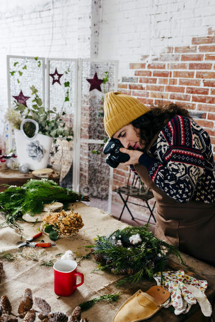Seitenansicht einer Frau beim Fotografieren der Blumenkomposition auf dem Tisch im Blumenladen — Stockfoto