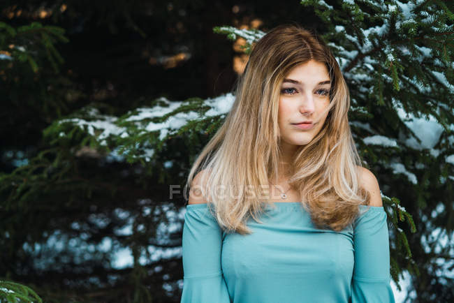 Portrait of young blonde woman standing at tree covered with snow and looking away — Stock Photo