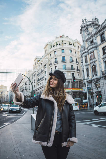 Portrait of young woman in cap taking selfie on street — Stock Photo