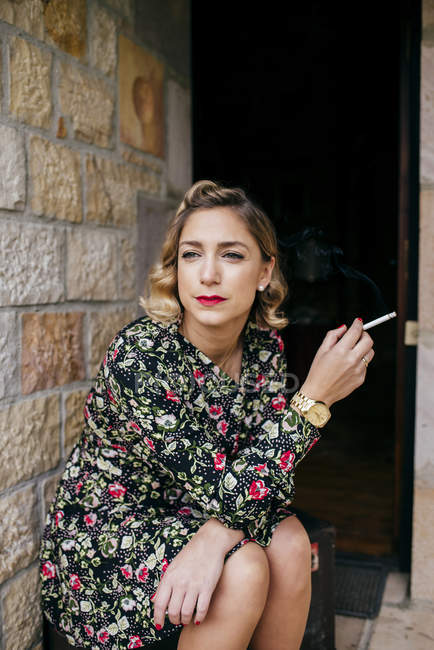 Retrato de mujer pensativa sentada en el porche y fumando cigarrillo . - foto de stock