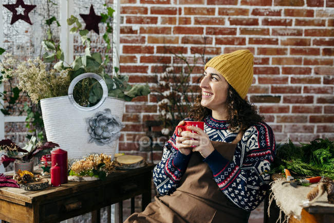 Retrato de mujer sonriente bebiendo bebida caliente en atelier floral - foto de stock