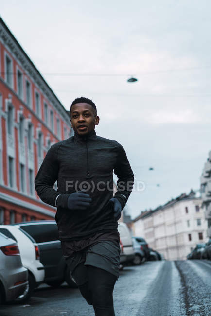Front view of athletic man in warm sportswear running on street — Stock Photo