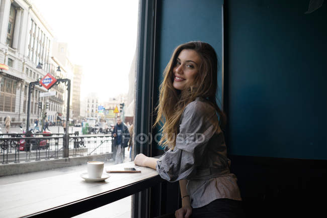 Jovem mulher bonita sentada no café e olhando sobre o ombro na câmera — Fotografia de Stock