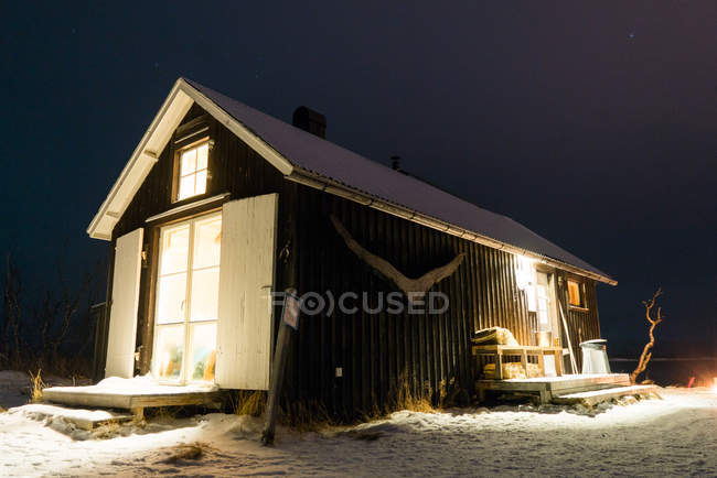 Зовнішній вигляд освітленої дерев'яної будівлі в зимовому лісі — стокове фото