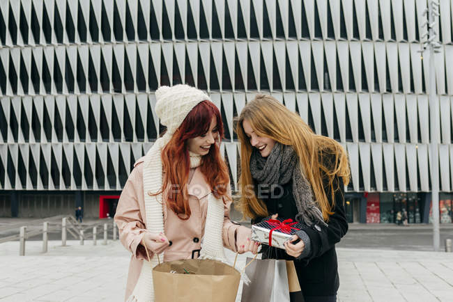 Front view of redhead girl giving gift to girlfriend at street scene — Stock Photo