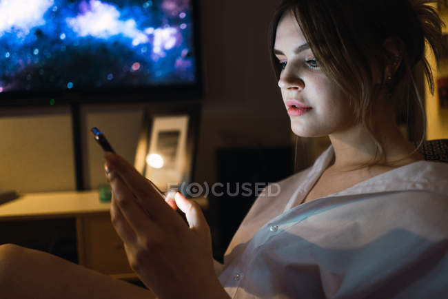 Vista lateral da mulher que navega smartphone em casa à noite — Fotografia de Stock