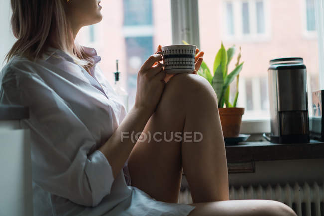 Обрізати жінку з чашкою, сидячи біля вікна — стокове фото