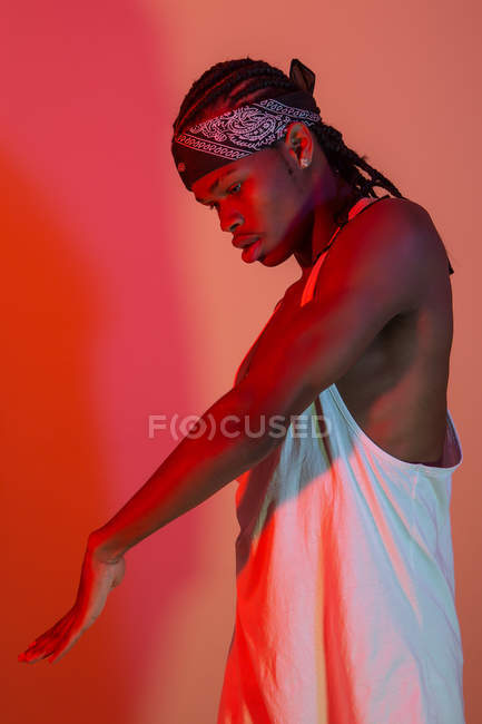 Vista laterale di uomo nero in do-rag guardando braccio teso in studio illuminato rosso — Foto stock