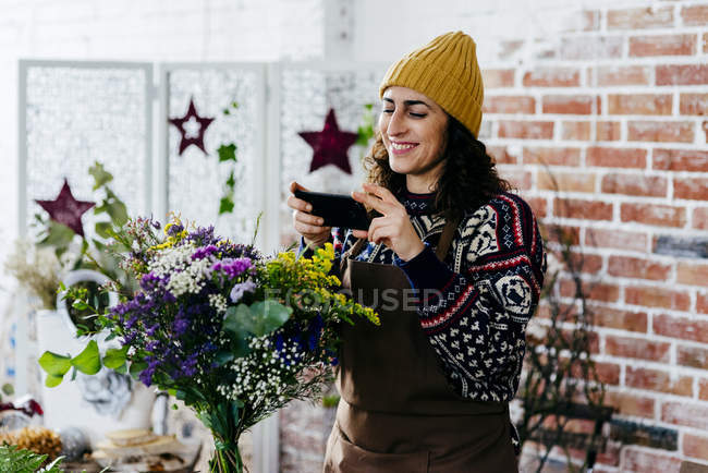 Portrait of smiling woman in hat taking photo of bouquet — Stock Photo