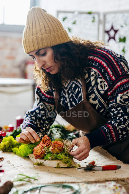 Портрет женщины в вязаном свитере и шляпе, создающей цветочную композицию — стоковое фото