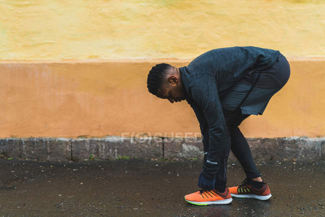 Seitenansicht des sportlichen Mannes im Stehen und Schnürsenkeln an Turnschuhen vor dem Joggen — Stockfoto
