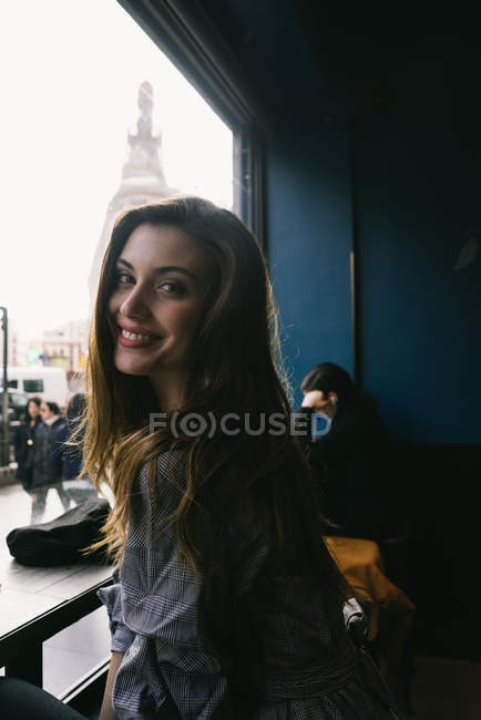 Young brunette woman looking over shoulder at camera in city cafe — Stock Photo