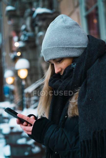 Vue latérale du jeune blondeoman à l'aide d'un smartphone sur la rue d'hiver — Photo de stock