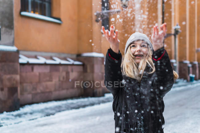 Portrait de femme blonde en vêtements chauds vomissant de la neige et ayant sur la rue enneigée . — Photo de stock