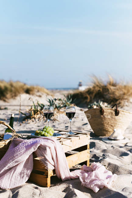 Still life of glasses with wine and plate with white grape on crate at summer beach. — Stock Photo