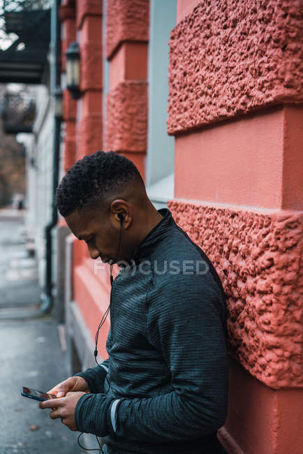 Side view of man with earphones listening music and looking at smartphone in hands — Stock Photo