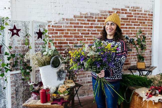 Portrait of smiling woman in knitted sweater holding bouquet and looking at camera — Stock Photo