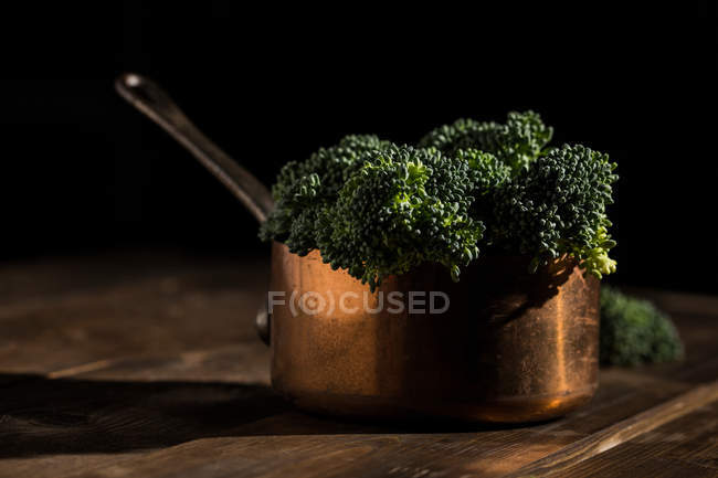Still life of fresh bimi broccolis in copper sauce pot on rustic wooden table — Stock Photo