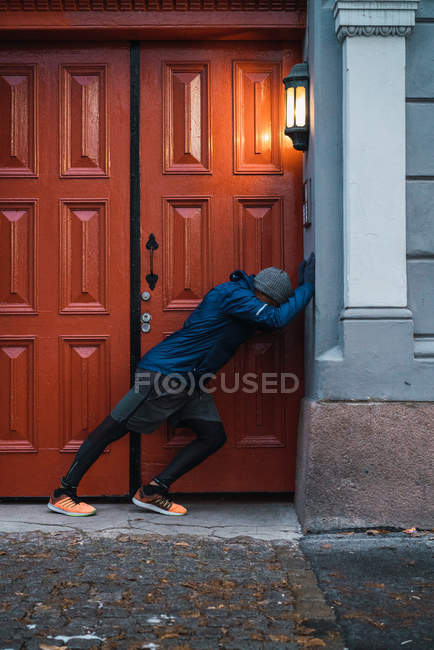 Side view of black man leaning at building facade and stretching muscles — Stock Photo