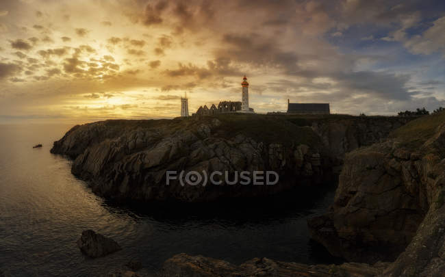 Vue lointaine vers le phare placé sur la colline au bord de la mer dans les lumières du coucher du soleil . — Photo de stock