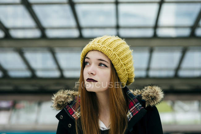 Portrait of young woman in coat and knitted hat posing in mall — Stock Photo