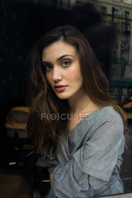Portrait  of brunette woman looking through window glass at camera — Stock Photo