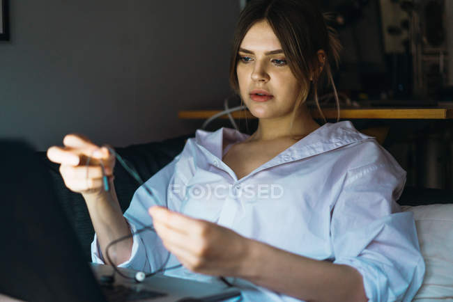 Retrato de mulher deitada com laptop e colocando fones de ouvido — Fotografia de Stock
