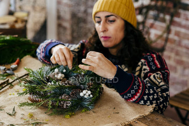 Portrait of woman squatting at table and making Christmas wreath — Stock Photo