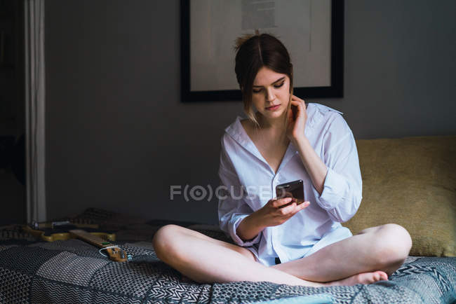 Ritratto di donna seduta a letto e smartphone di navigazione — Foto stock