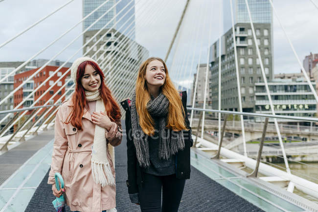 Vista frontal de dos mujeres sonrientes caminando por el puente - foto de stock