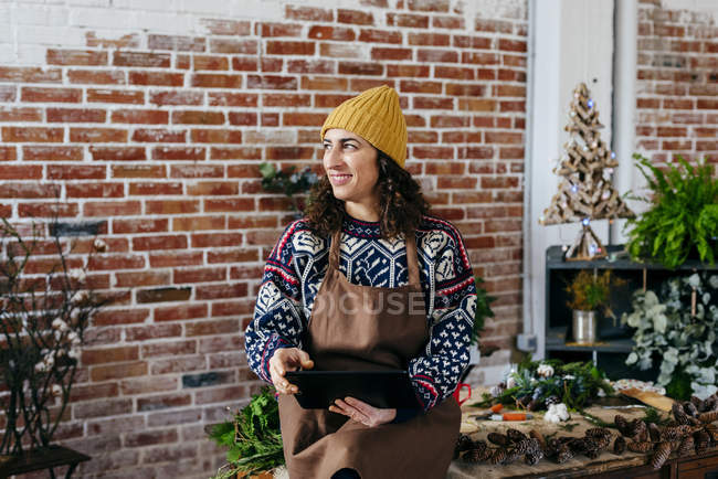 Портрет женщины в вязаном свитере и шляпе с помощью планшета и глядя в сторону цветочного ателье — стоковое фото