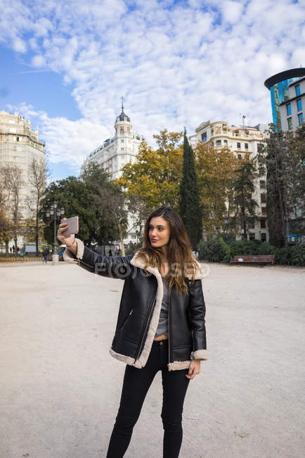 Женщина в теплом пальто делает селфи со смартфоном в парке — стоковое фото
