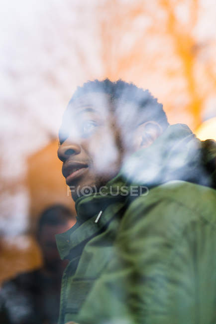 Портрет человека в теплой одежде, смотрящего на улицу через окно . — стоковое фото