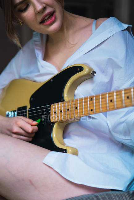 Обрізати жінку, граючи на гітарі на дивані — стокове фото