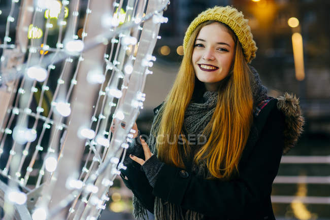 Porträt einer lächelnden Frau mit gelber Strickmütze, die bei der Beleuchtung posiert — Stockfoto