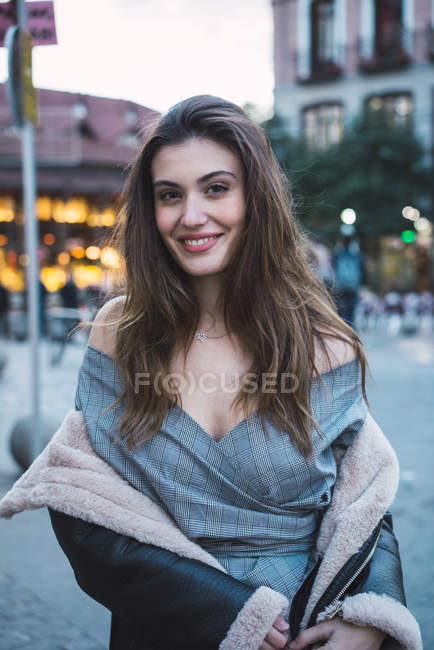 Portrait of smiling brunette woman taking of coat on street and looking at camera — Stock Photo