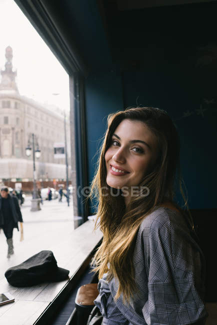Портрет молодой красивой женщины, позирующей у окна кафе и смотрящей в камеру — стоковое фото