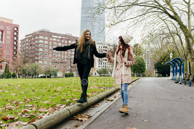 Rotschopf Mädchen hilft Freundin beim Balancieren beim Gehen auf Kante — Stockfoto