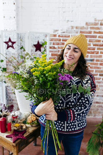Усміхнена жінка в в'язаному светрі і капелюсі розставляє квіти — стокове фото