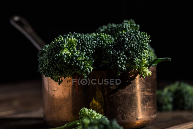 Bodegón de broccolis bimi fresco en maceta de salsa de cobre sobre mesa de madera - foto de stock