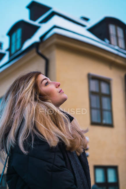 Side view of dreamy blonde woman looking up at winter street scene — Stock Photo