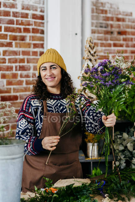 Femme souriante en pull tricoté et chapeau posant avec un joli bouquet — Photo de stock