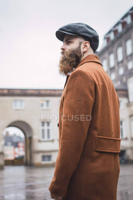 Vista lateral del hombre barbudo de abrigo caminando por la ciudad - foto de stock