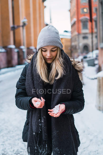 Porträt eines blonden Mädchens, das bei winterlichen Straßenverhältnissen den Schnee in Händen betrachtet — Stockfoto
