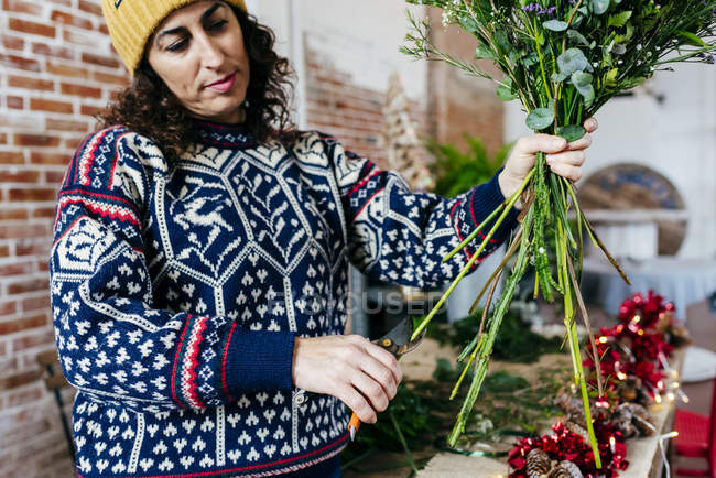Portrait de femme en pull tricoté et chapeau coupant des brindilles de fleurs — Photo de stock