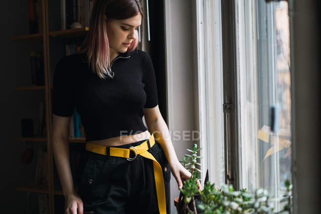 Portrait of woman looking down at plants on window sill — Stock Photo
