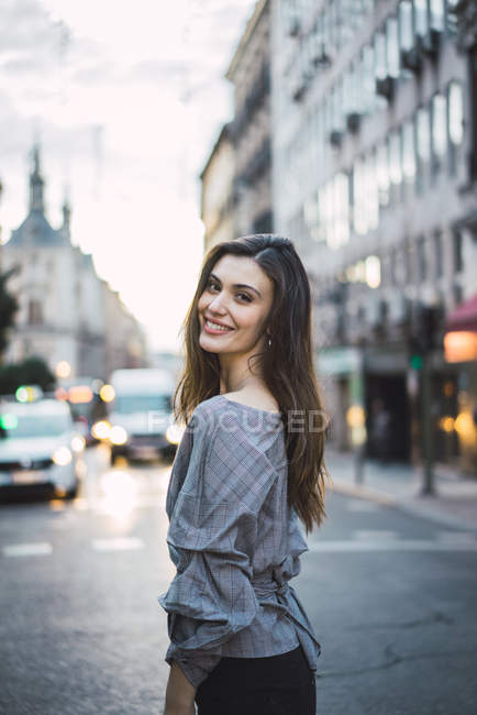 Vue latérale de la femme brune posant sur la rue urbaine et regardant la caméra — Photo de stock